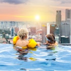 Children in a rooftop swimming pool looking at the Singapore skyline